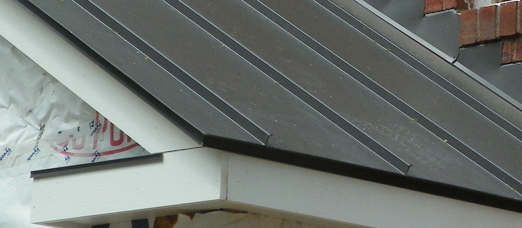 Hand-fabricated step flashing where a standing seam metal roof meets a brick chimney, with a clean folded rake and eave edge