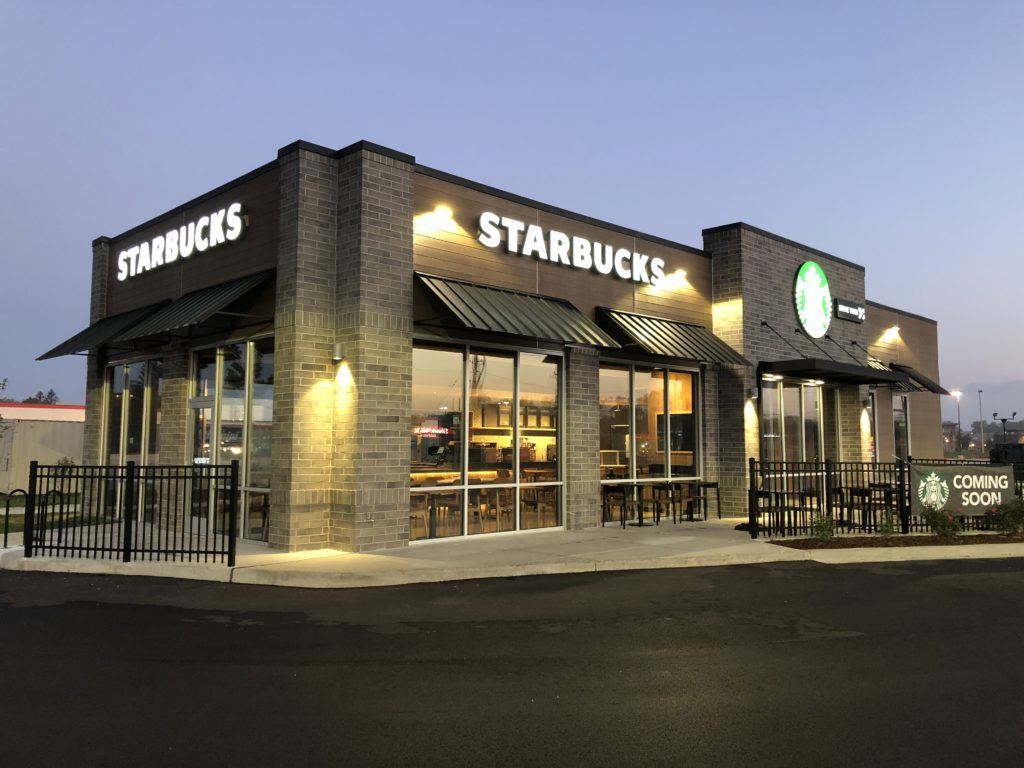 Dark bronze standing seam metal awnings on a Starbucks coffee storefront at dusk