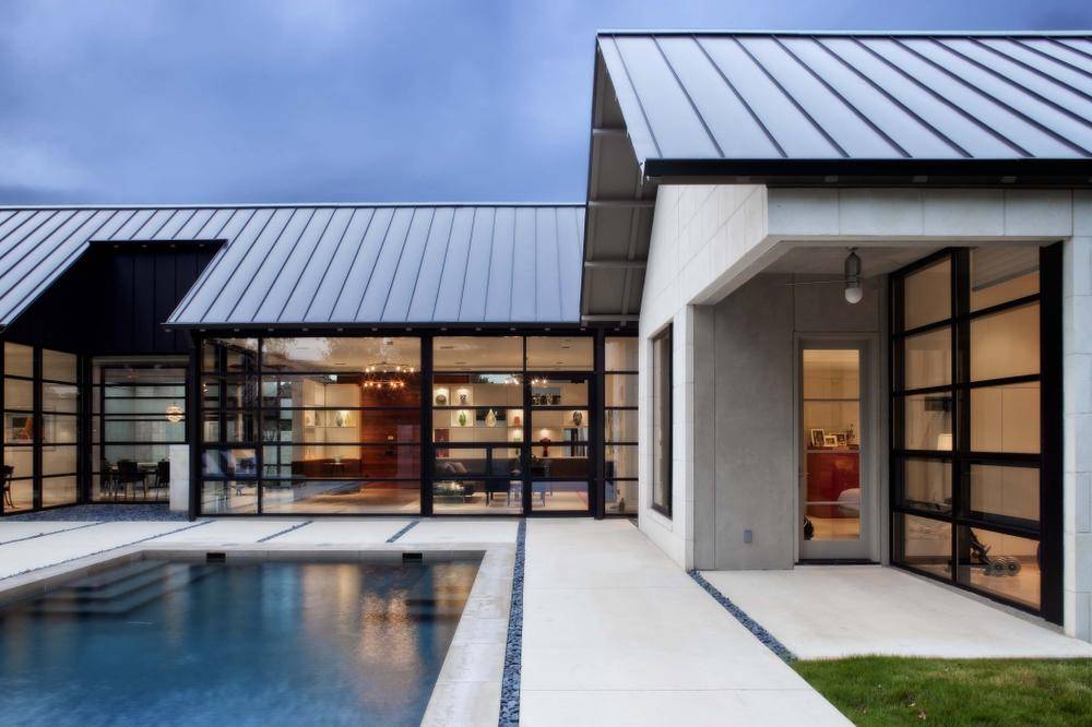 Silver standing seam metal roof on a glass-walled modern home with a courtyard pool at dusk in Beverly Hills