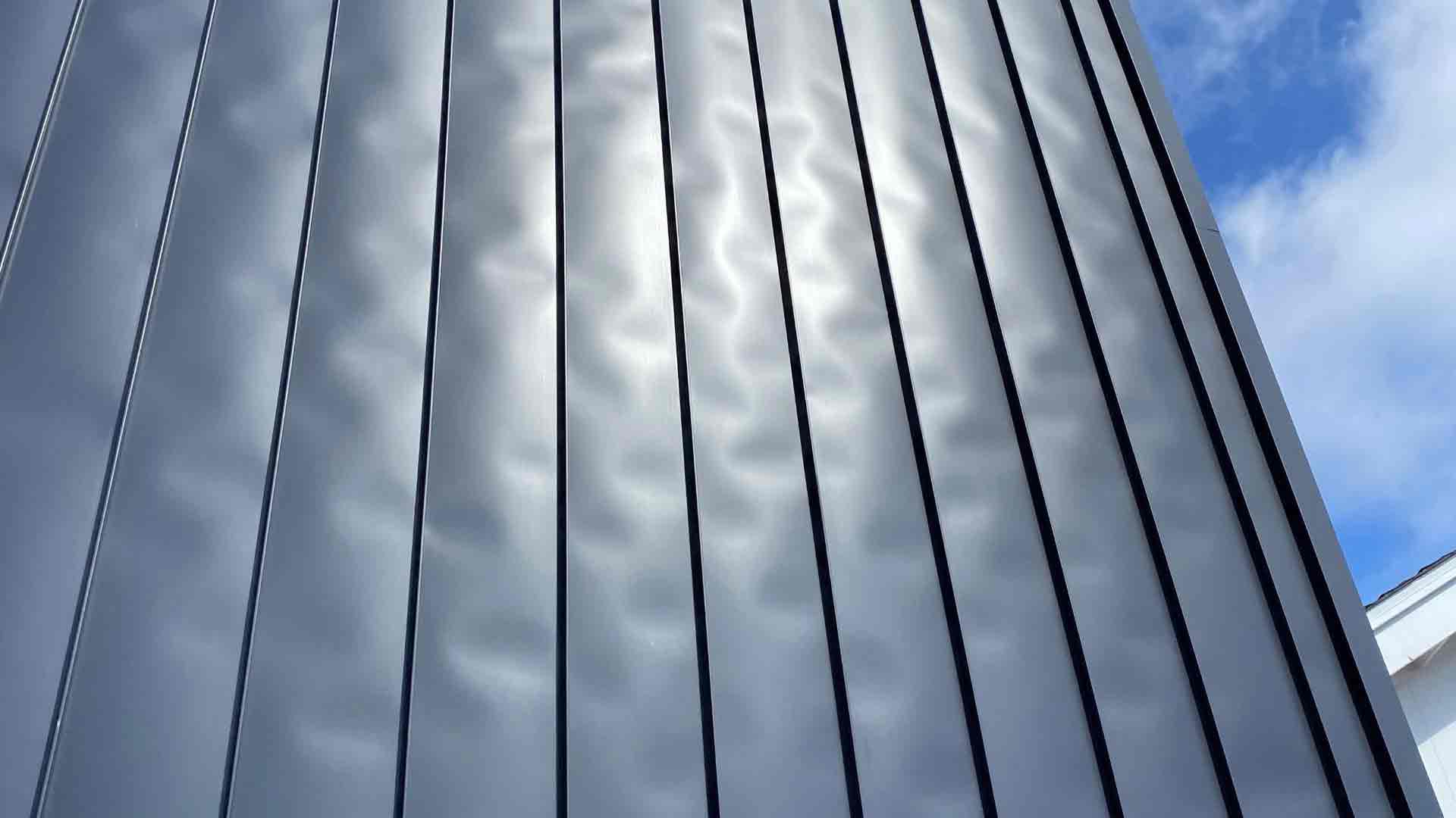 Visible oil canning on a thin-gauge standing seam metal roof in low-angle sunlight